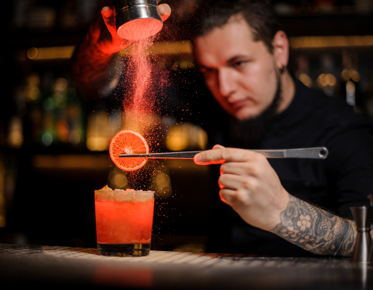 Ein Mann mixt hinter der Bar einen Cocktail mit einer Orangendust-Garnitur.