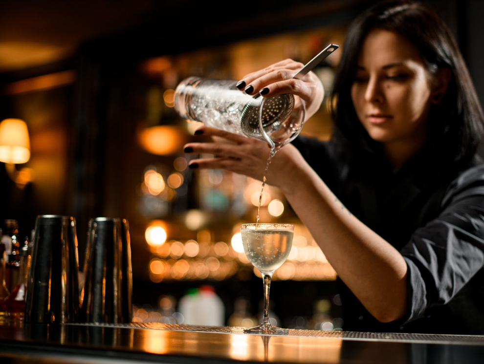Mujer bartender de DBA sirviendo un cocktail a través de un colador en una copa de cóctel clásica. 
