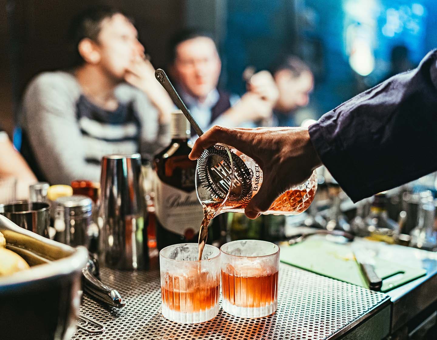  Der Barkeeper schenkt Cocktails mit Rum in zwei Gläser ein