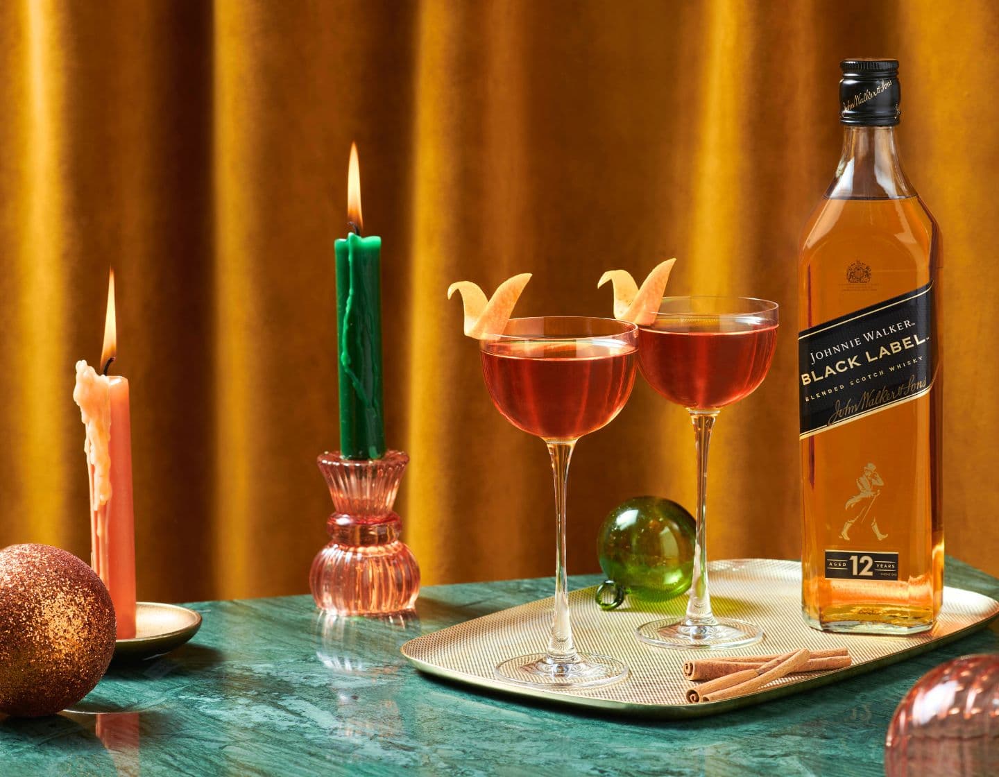 Cocktail in a coupe glass with orange garnish, surrounded by bottle of Johnnie Walker Black Label Whisky, and candles.