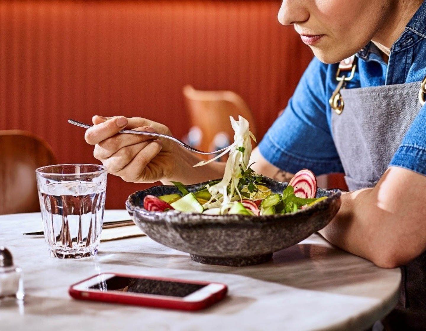 Mujer comiendo una ensalada y descansando de un ajetreado turno de trabajo en un restaurante o bar.