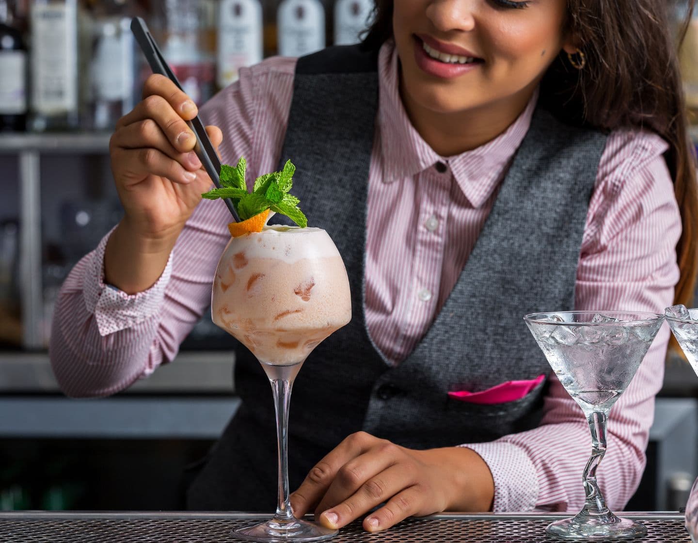 Bartender garnishing a frozen cocktail with mint and orange. 