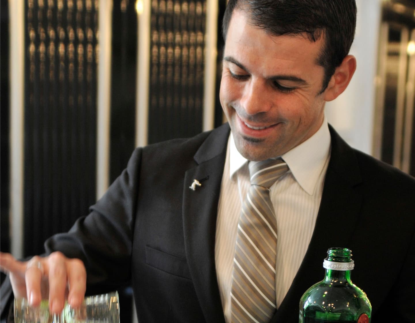 Ago Perrone in a suit measuring a cocktail