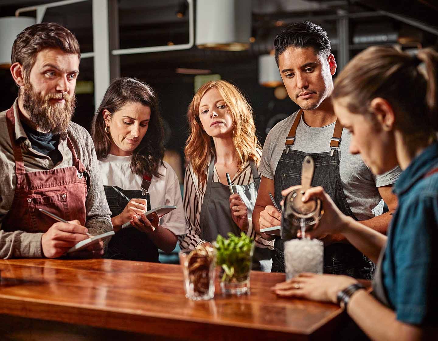 Barkeeper:innen versammelten sich um einen Tisch und erhalten eine Schulung zur Cocktailzubereitung.