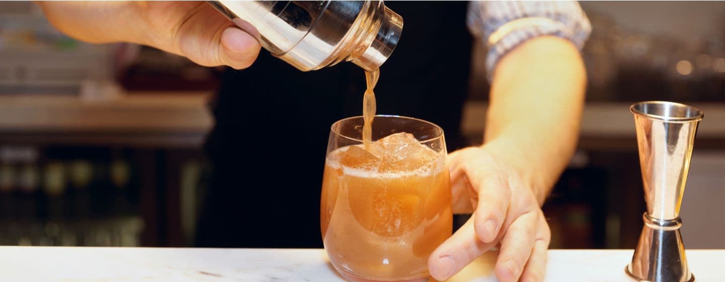 Imagem de um bartender servindo um coquetél pela coqueteleira