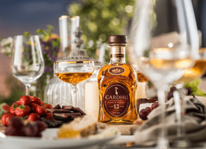 Bottle of Cardhu set in centre of a table beside plates of food and glasses