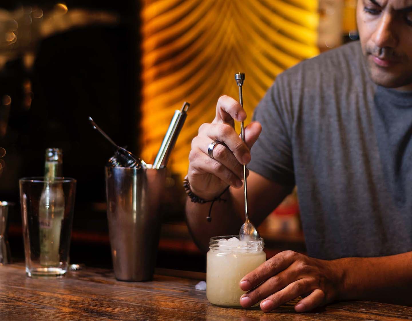 Ein Mann rührt einen Cocktail mit einem langstieligen Rührlöffel.