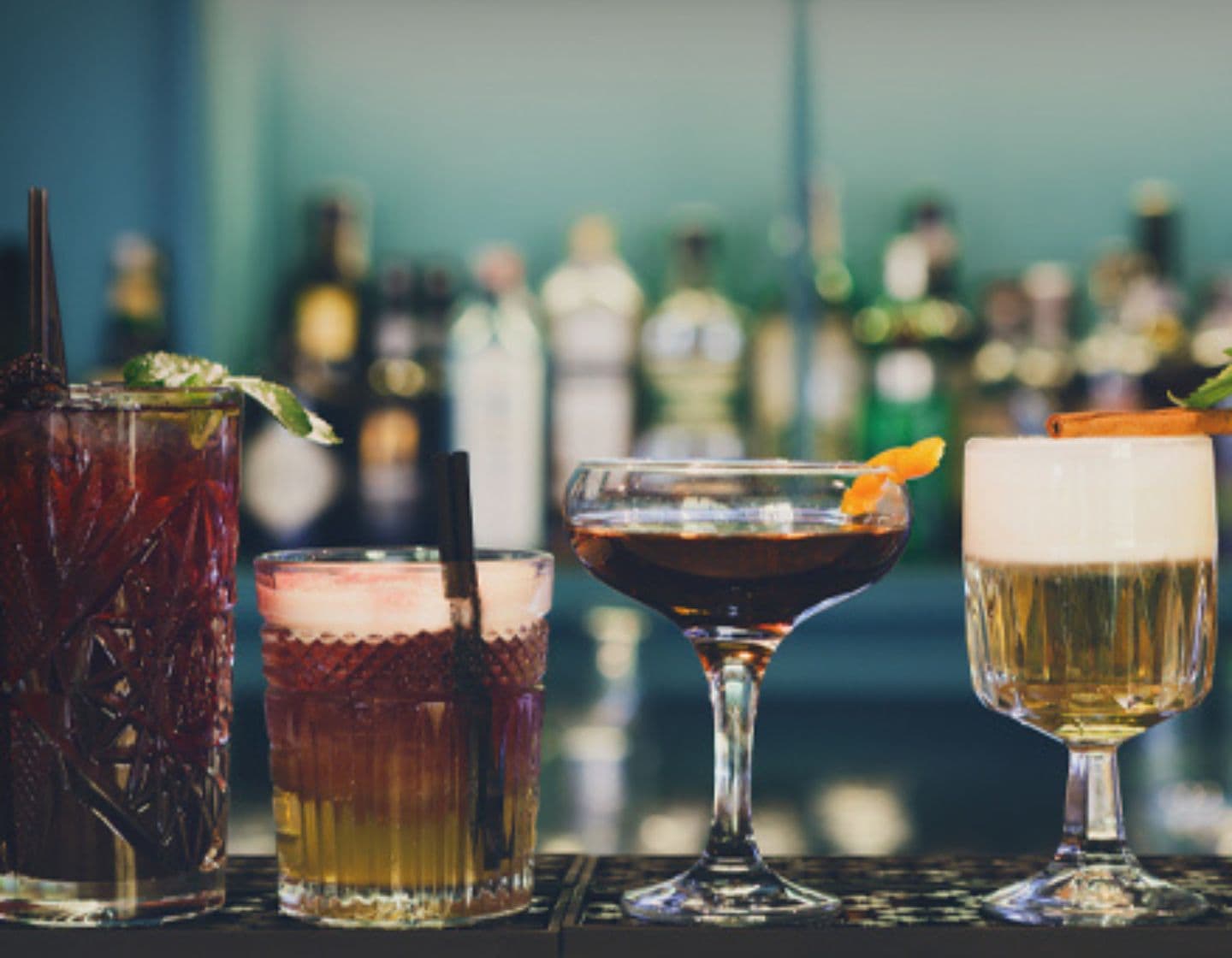 Four different garnished cocktails lined along a bar.