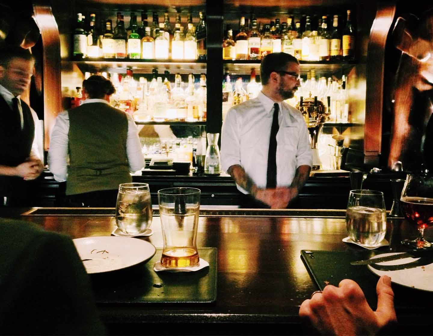 Barpersonal arbeitet hinter der belebten Bar, während Kunden an der Bar sitzen und Essen und Getränke genießen.