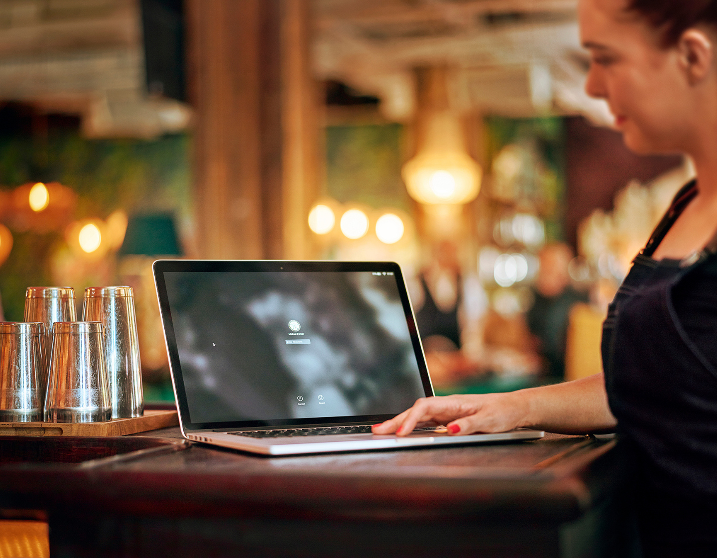 Woman standing in a bar setting holding a laptop 