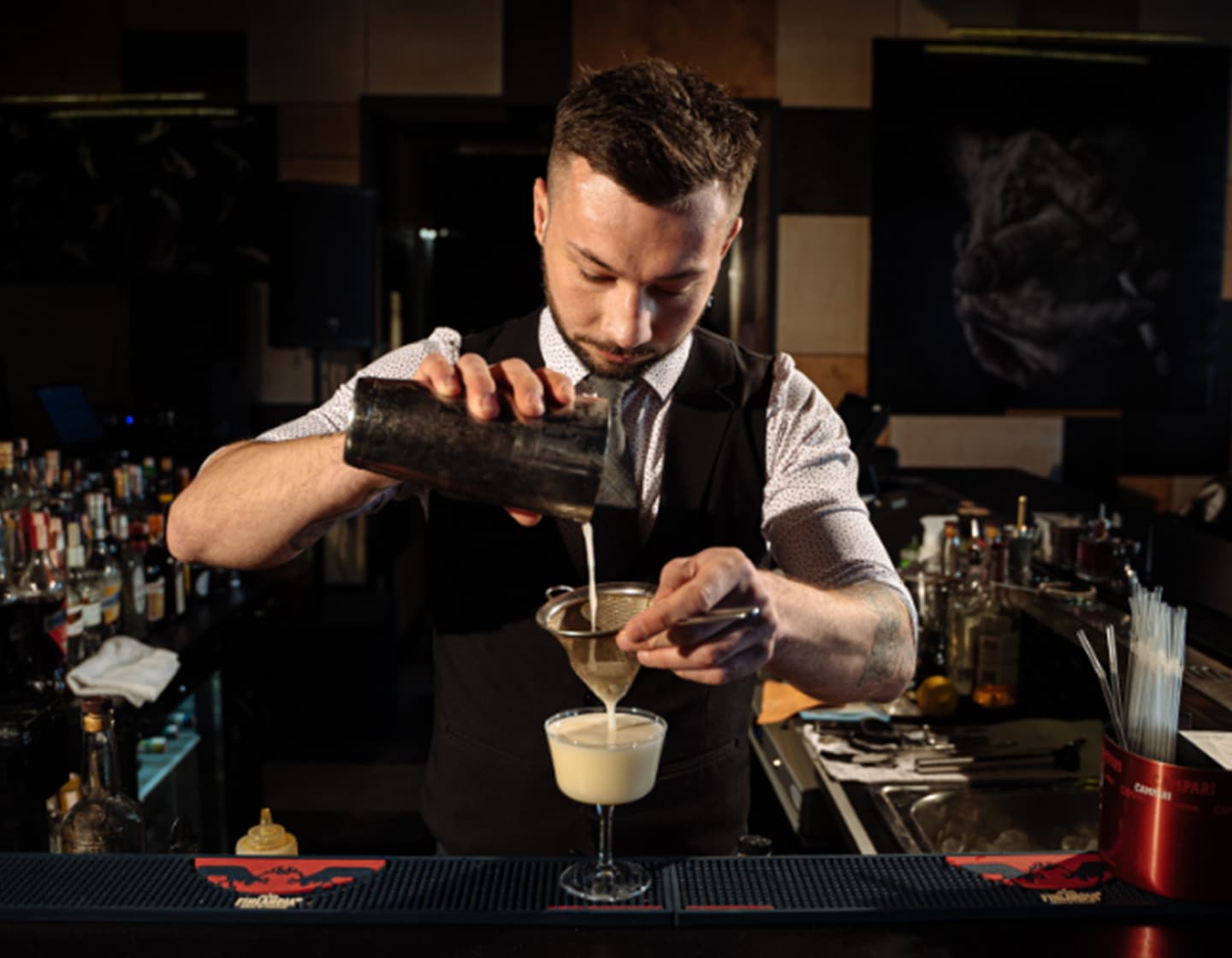 Ein Barkeeper gießt einen Cocktail durch ein Sieb in ein Glas. 