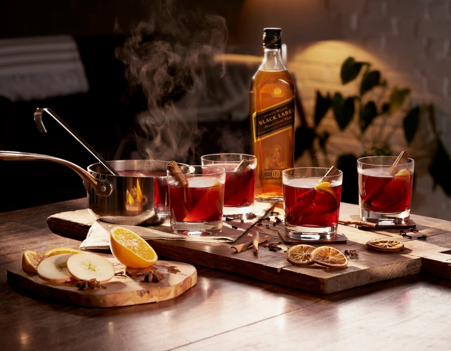 Bottle of Johnnie Walker black label next to four hot toddies and a steaming saucepan