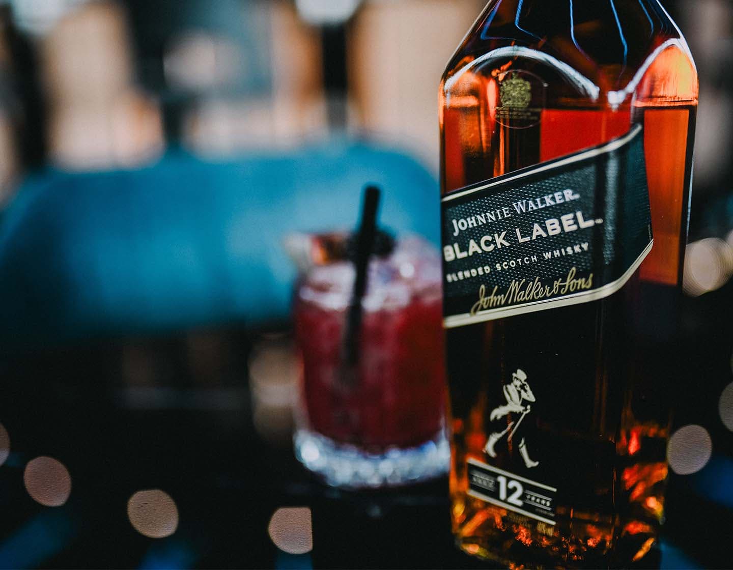 Close shot of a bottle of Johnnie Walker Black Label with a red/pink cocktail in the background