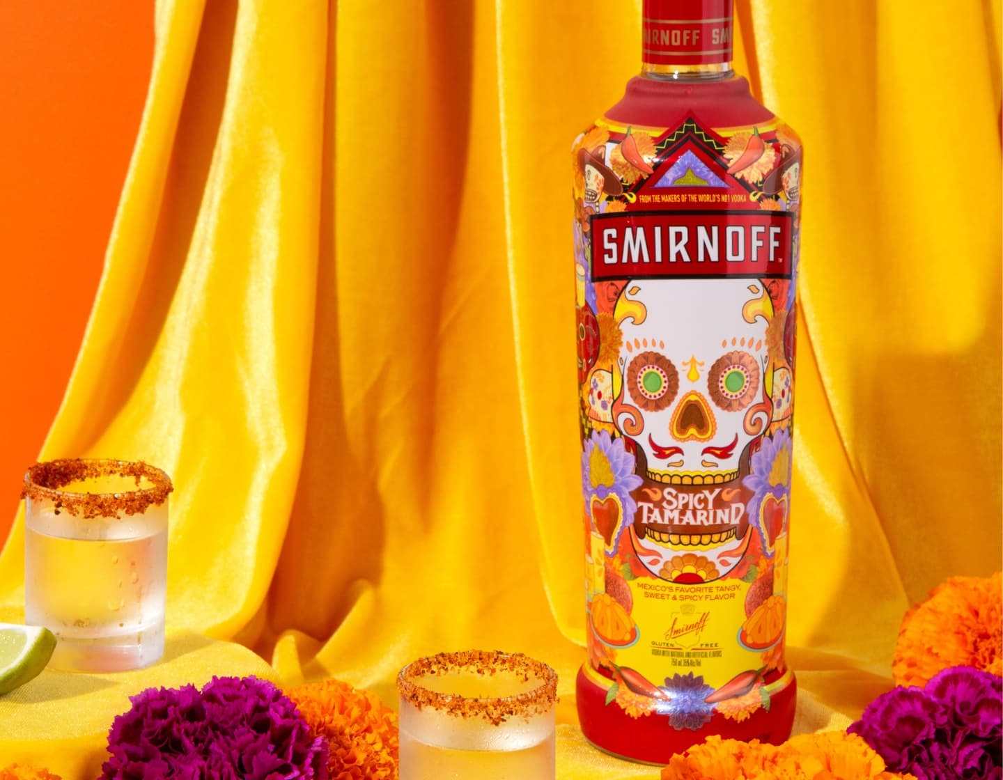 Bottle of Smirnoff Spicy Tamarind with two cocktails against yellow draped fabric