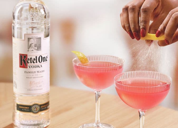 Ketel One bottle beside two pink cocktails being garnished with a spritz of fresh lime.