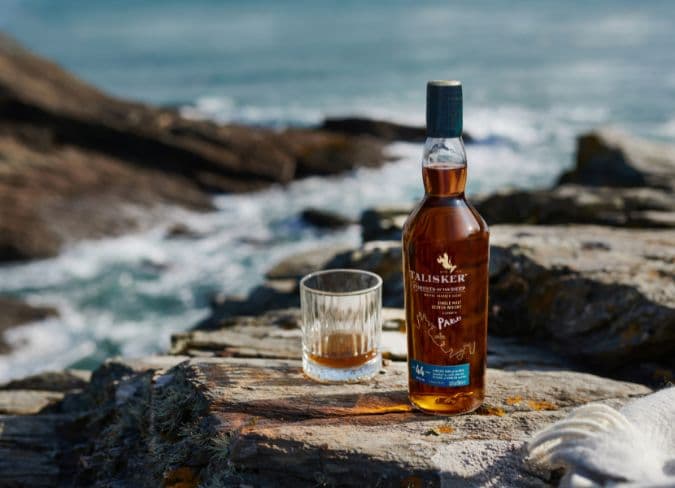 Talisker 45YO ao lado de um copo de whisky puro em uma costa rochosa da Escócia