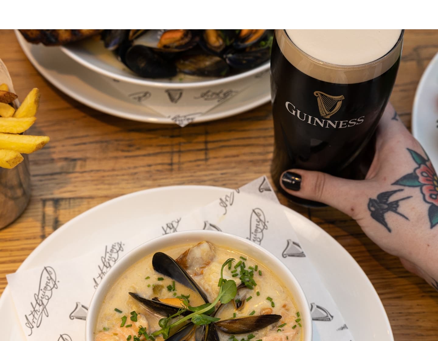 Hand holding a pint of Guinness next to a bowl of clam soup