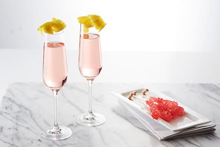 Two champagne flutes with pink champagne and garnish 