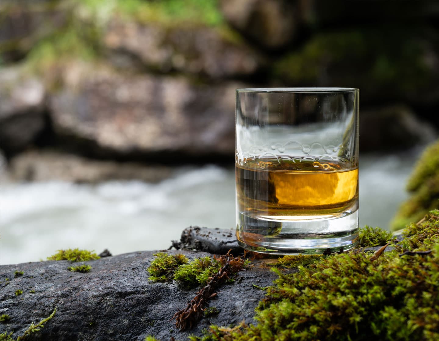 Vaso de whisky junto a un río con algo de musgo