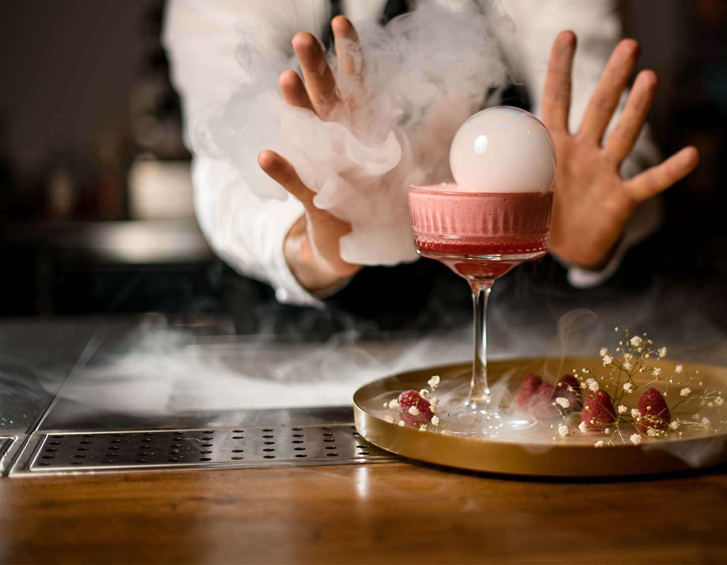 A bartender presenting a cocktail surrounded by a foggy smoke.  