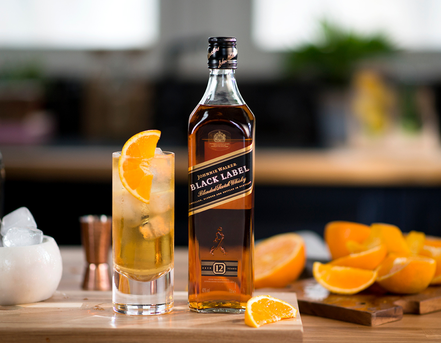 Bottle of Johnnie Walker Black Label whisky on chopping board beside cocktail surrounded by sliced oranges. 