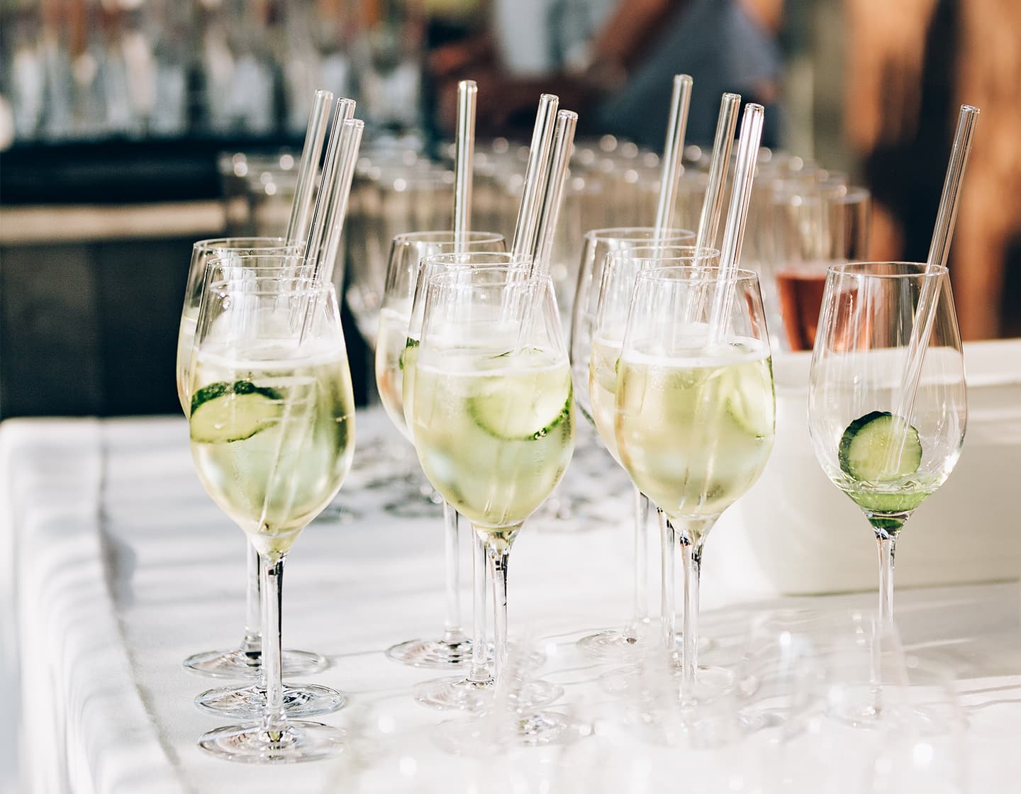 A group of identical apéritif glasses with glass straws and ice with a slice of cucumber.