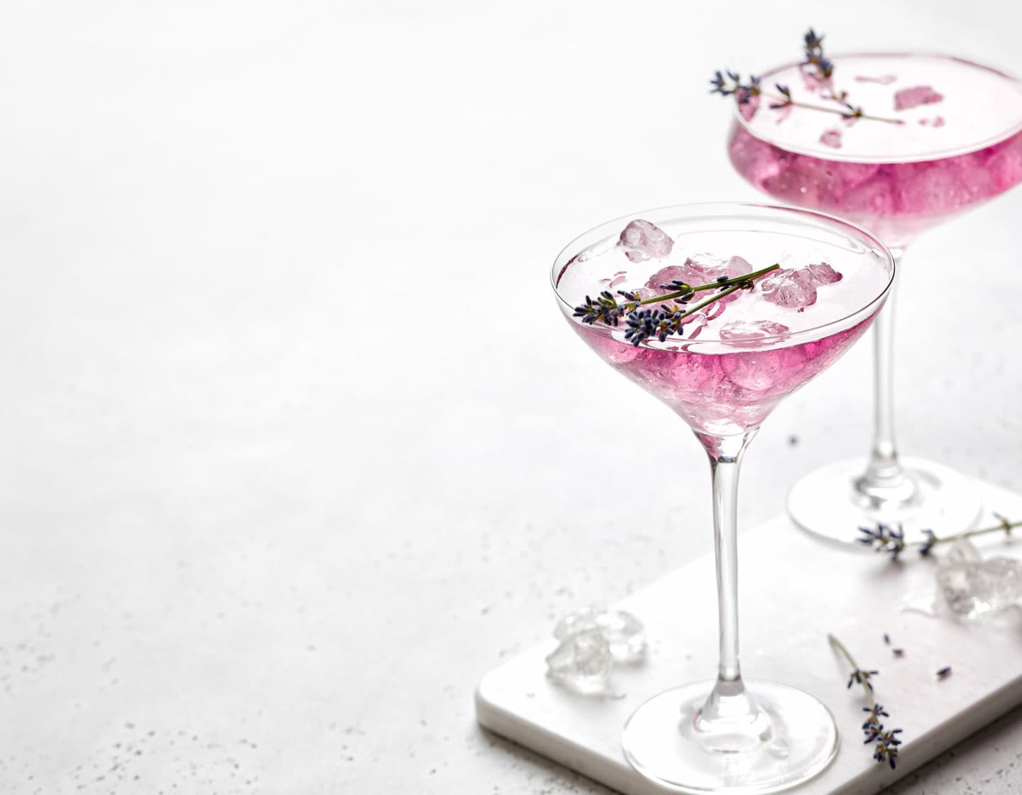 Dos copas de cócteles color rosa con cubos de hielo y adornado con flores