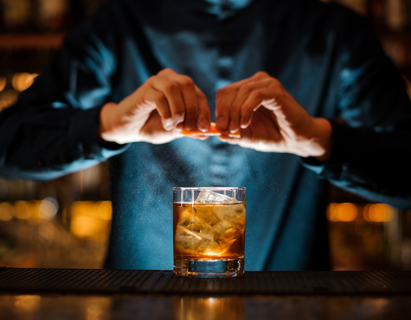 Hands squeezing orange into whisky cocktail