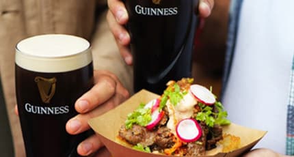 Dos vasos Guinness acompañado de comida que tiene carne y vegetales