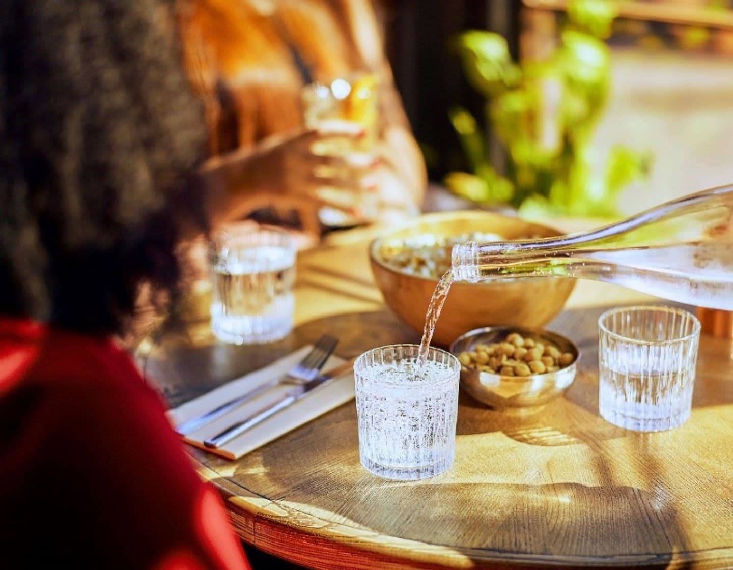 Drink being poured into a clear glass with food and small plates on the table