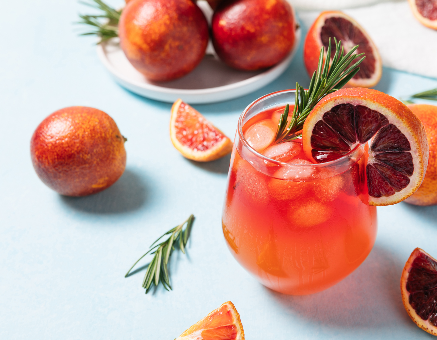 Tumbler-Glas mit alkoholfreiem Orangen-Cocktail, frischen Früchten und Garnitur