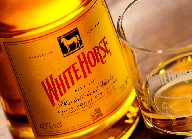 Botella de whisky White Horse sobre una mesa junto a un vaso de whisky solo 