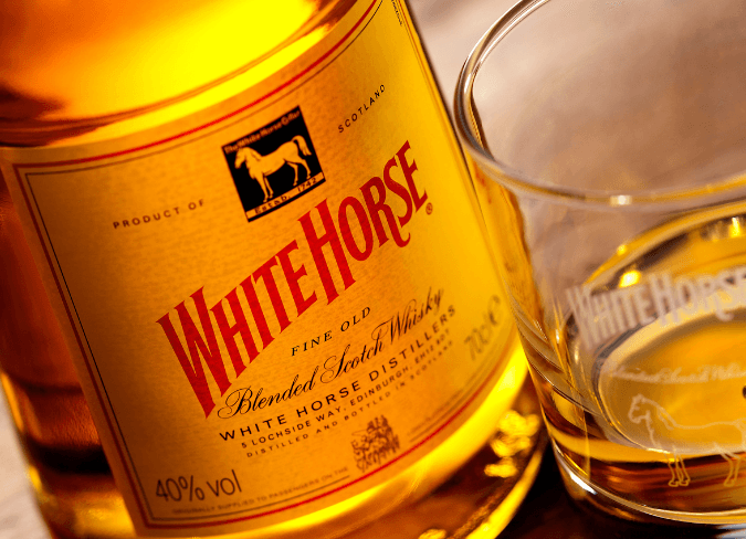 Eine Flasche White Horse Whisky auf einem Tisch neben einem Glas Whisky