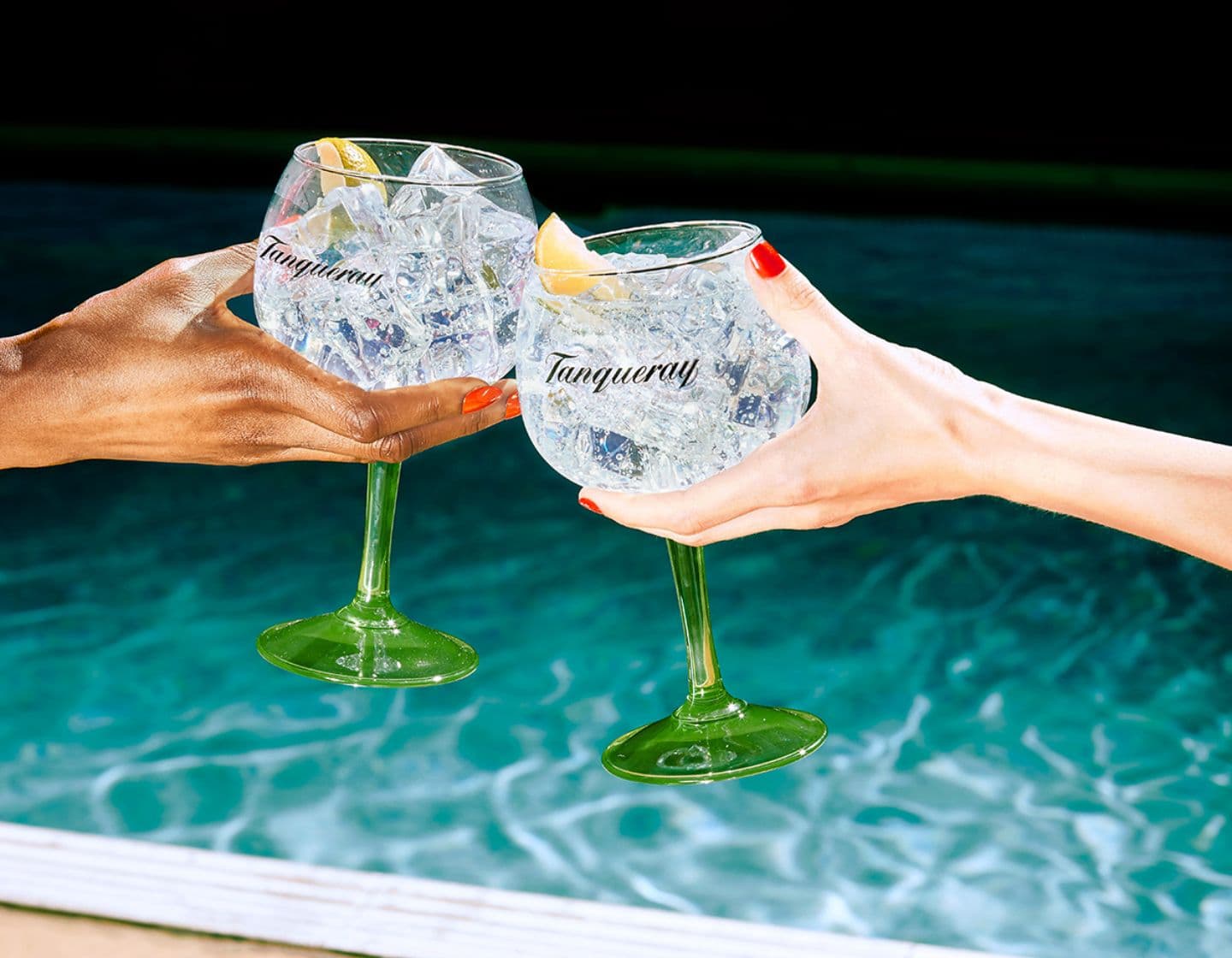 Dos personas chocan sus vasos de ginebra Tanqueray frente a una piscina. 