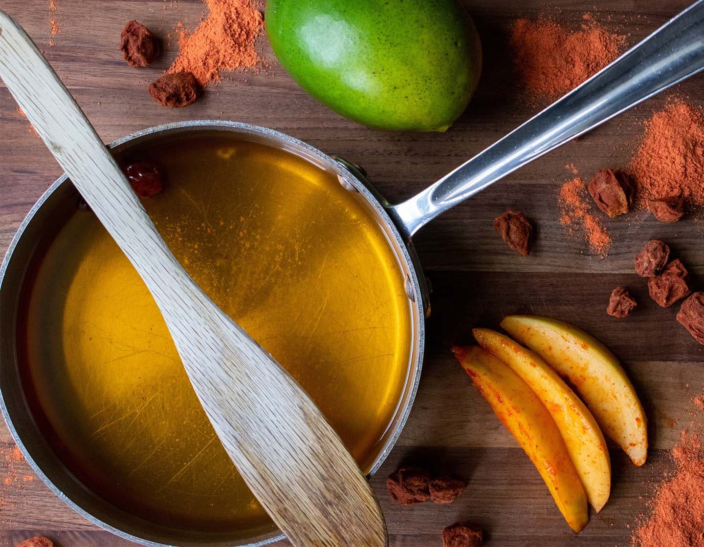 A saucepan with syrup surrounded by spices and mango. 