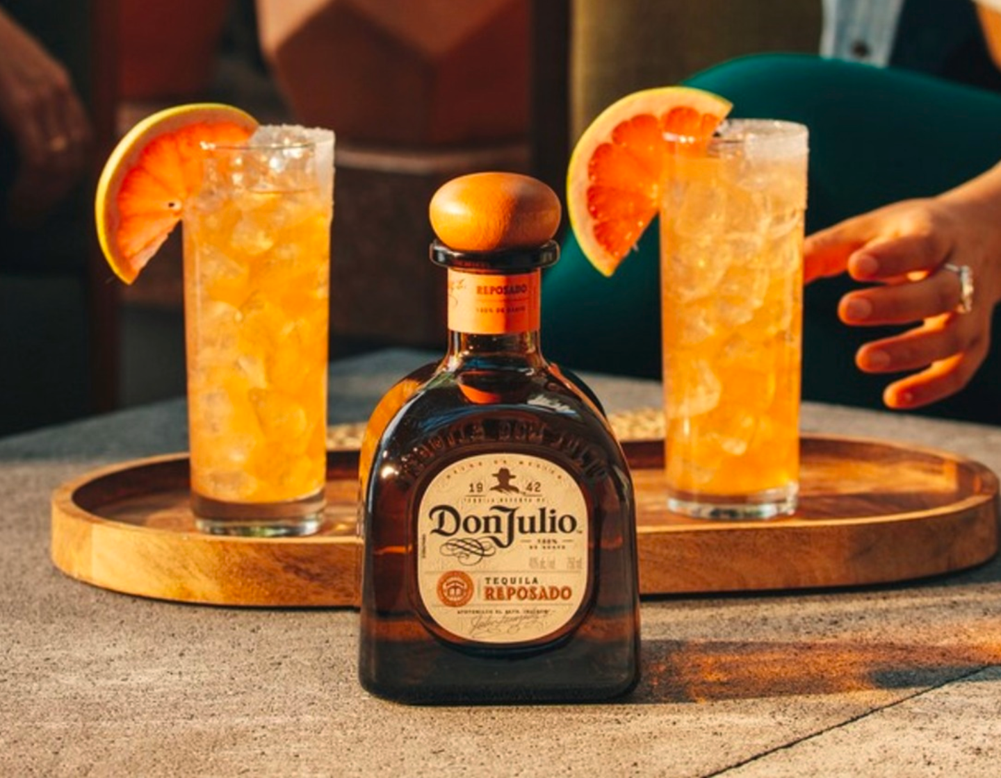 Bottle of Don Julio Reposado tequila in front of tray of two orange cocktails