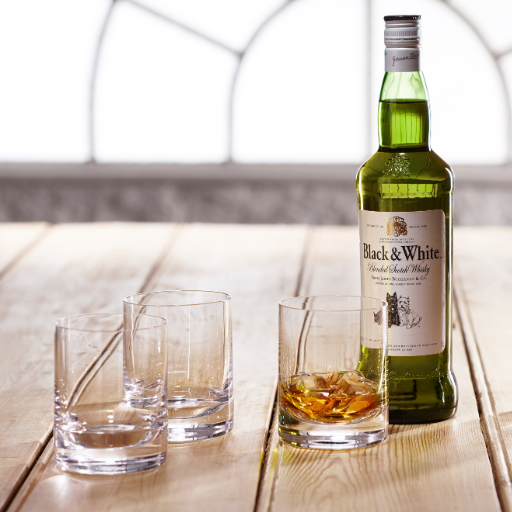 Una botella de Whisky Black & White en una mesa de madera acompañada por vasos de Whisky