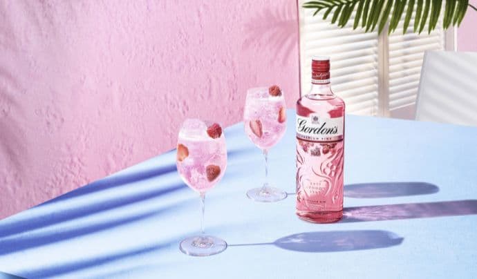 Gordons pink gin bottle accompanied by two garnished gin cocktails.