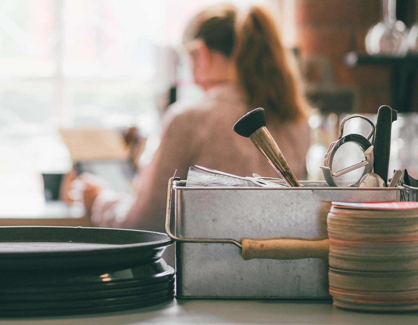 Muddling tools on a countertop, with a woman with her back turned in the background.  