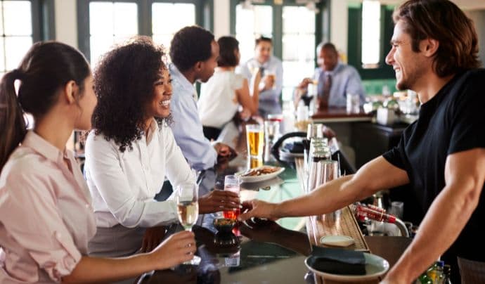 Camarero sirviendo bebidas a clientes sonrientes en un bar